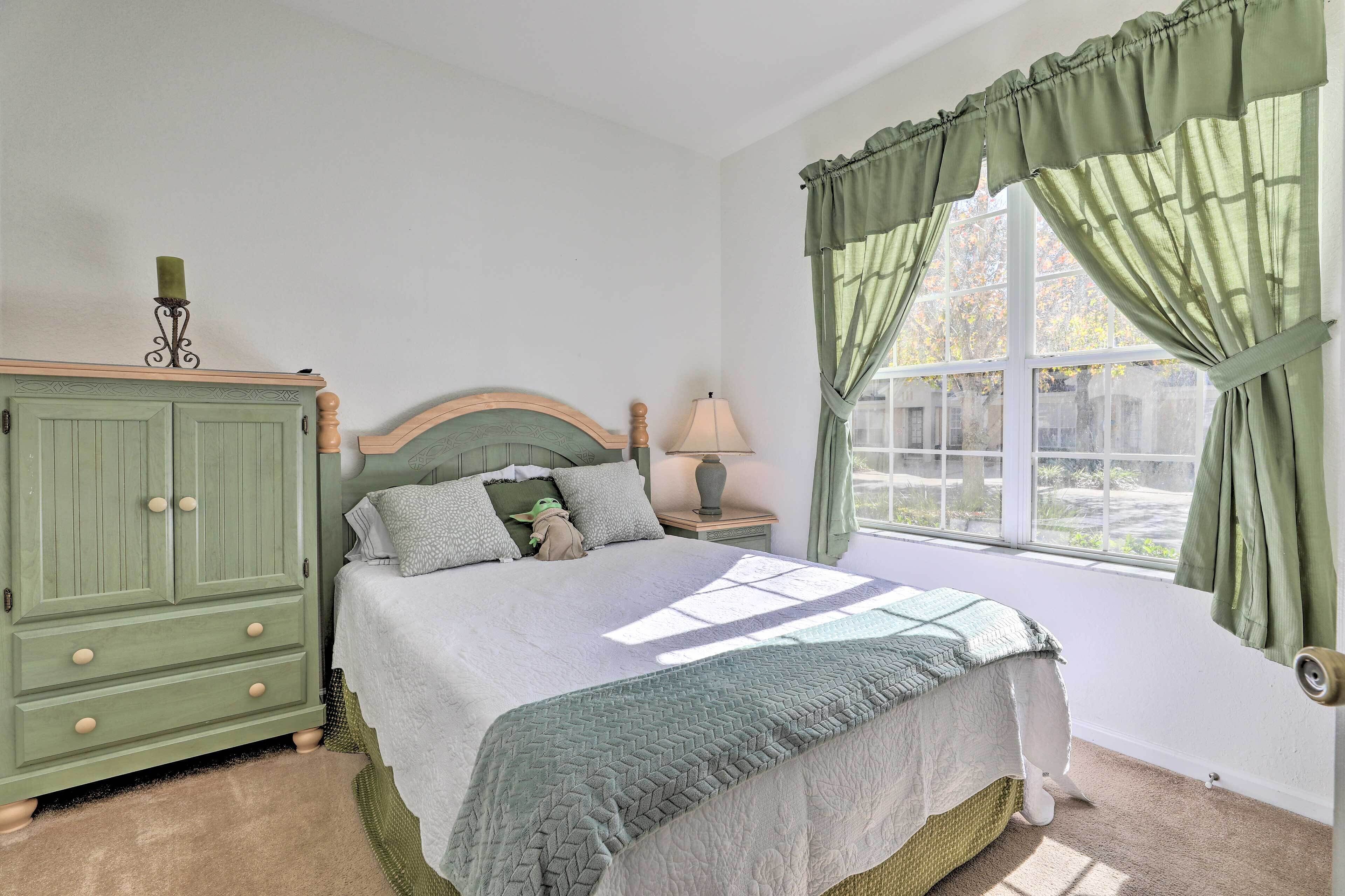 Une chambre à coucher avec un lit, une table de chevet, une lampe, une armoire et une fenêtre avec des rideaux.