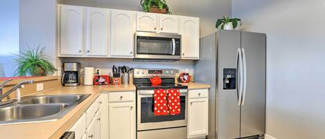A modern kitchen with white cabinets, stainless steel appliances, and a tiled floor.
