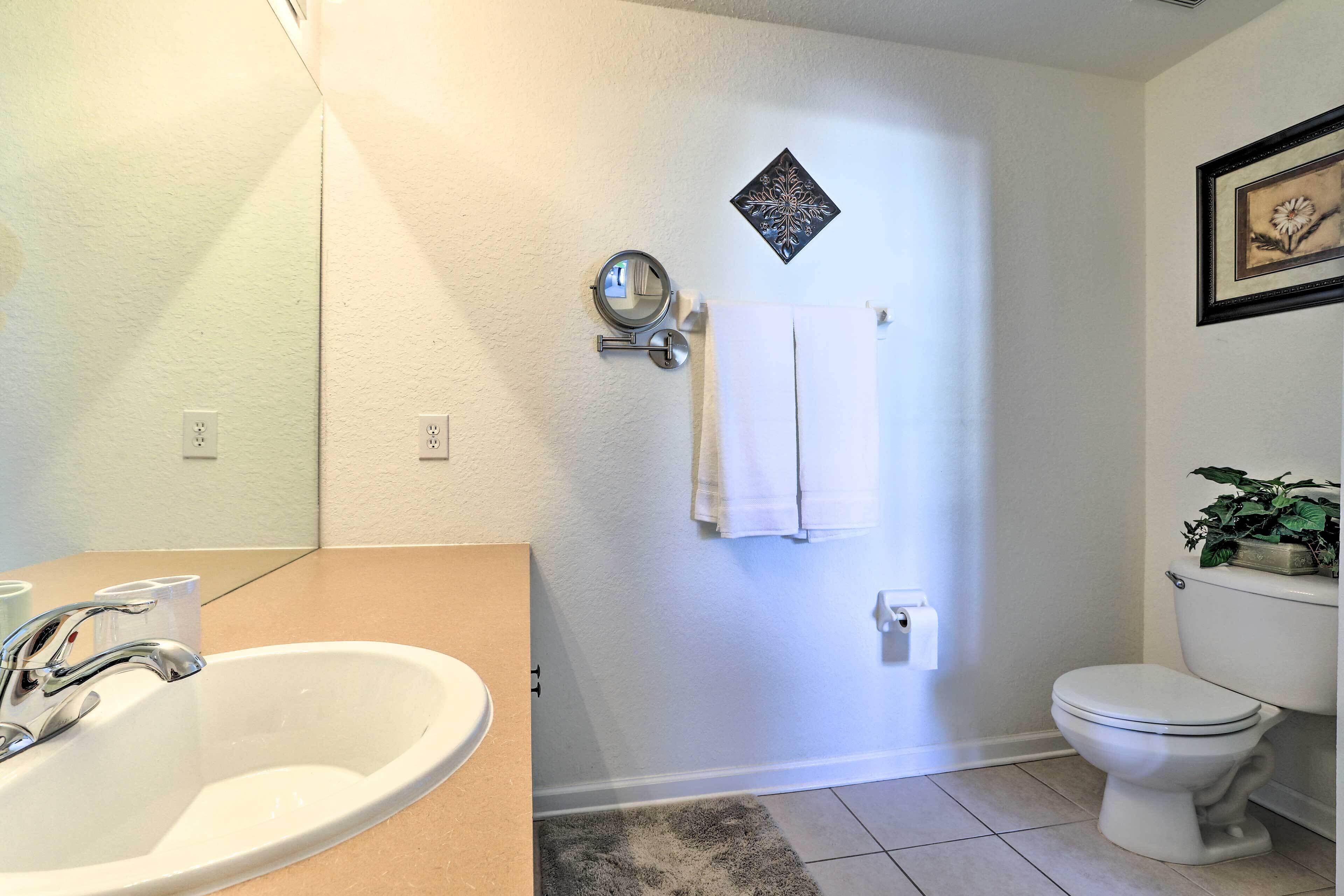Une salle de bain avec un lavabo, des toilettes et un miroir. On y trouve un porte-serviettes avec des serviettes et un tableau encadré accroché au mur.