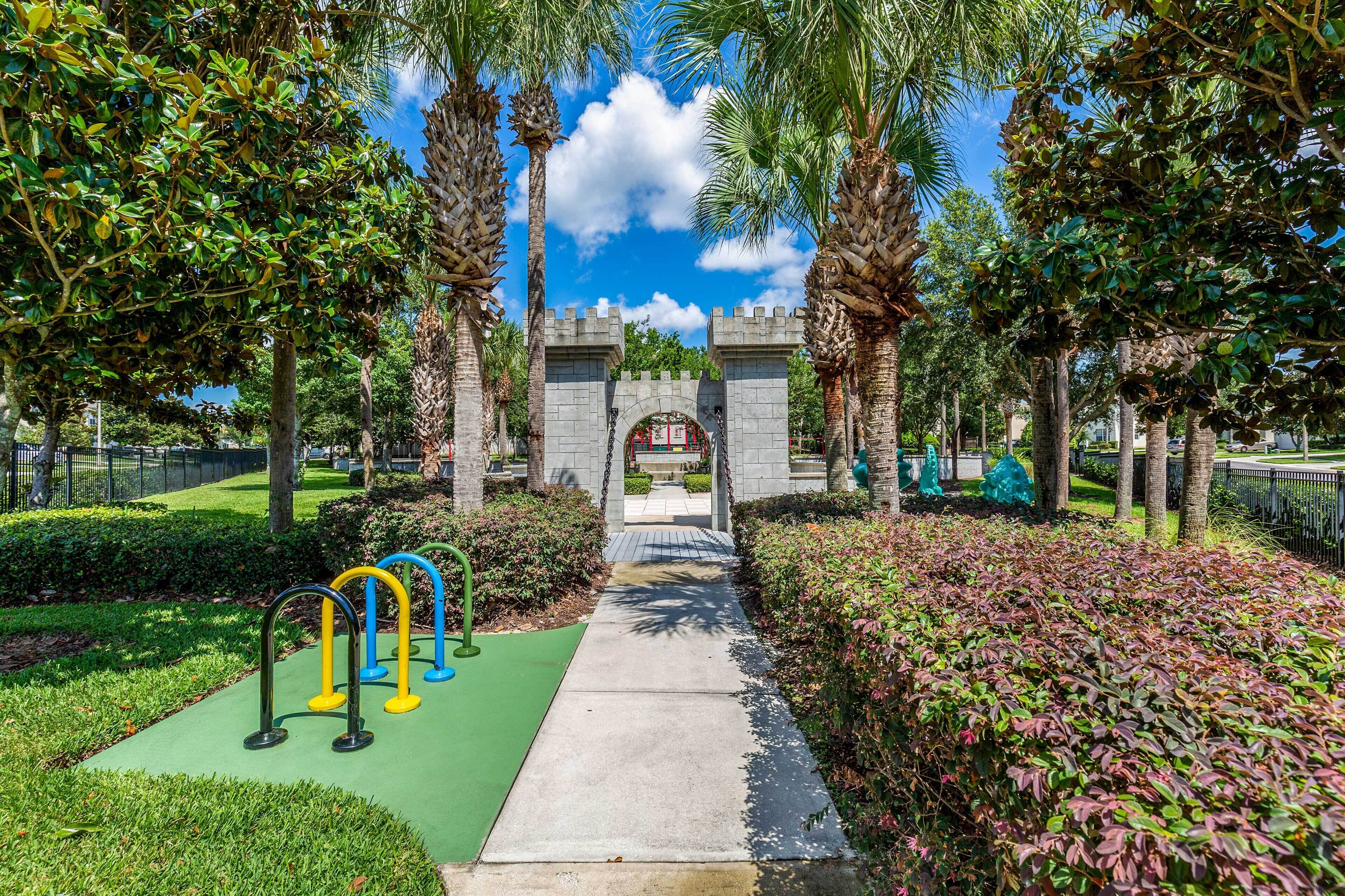 A pathway leading to a stone archway surrounded by palm trees and greenery.