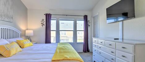 Een hotelkamer met een bed, een dressoir, een aan de muur bevestigde televisie en een raam met gordijnen.