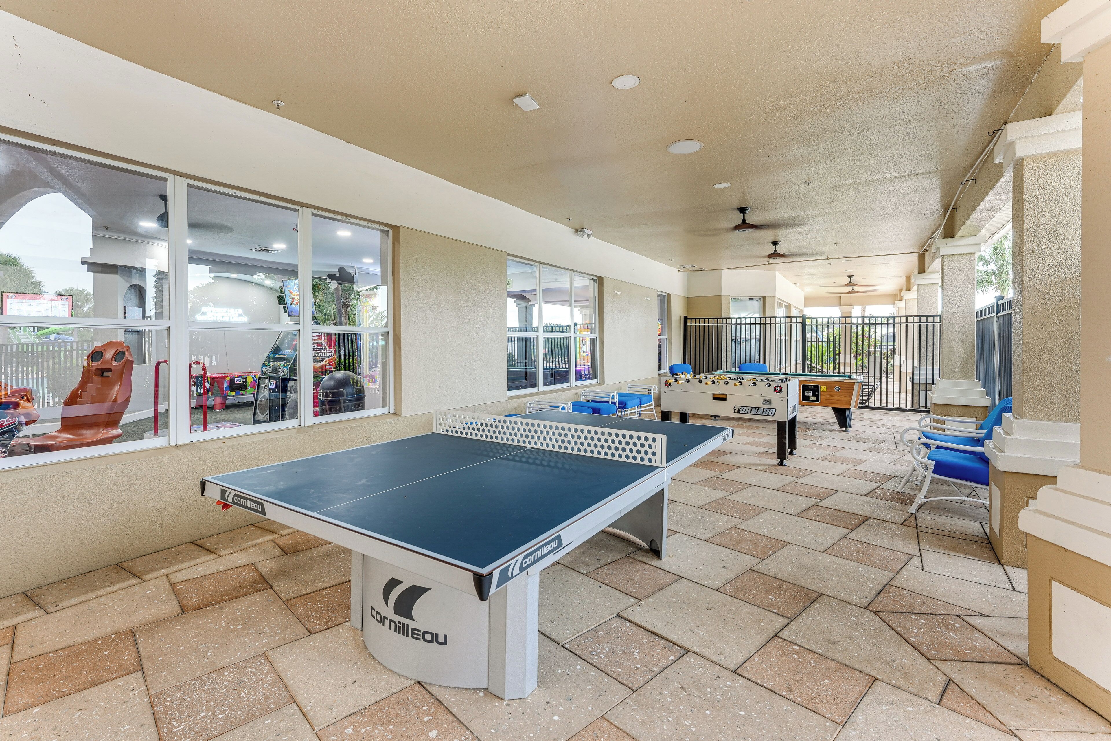 A covered outdoor area with a ping pong table, a foosball table, and blue chairs.