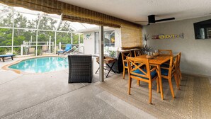 A poolside area with a dining table and chairs, a wicker chair, and a view of the pool. - Backyard Oasis! Waterfront Haven in Bradenton (Bradenton)