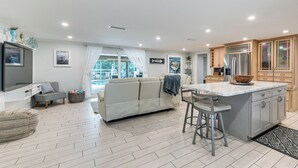 A modern kitchen with a central island, a dining area with a bar stool, a sofa, and a flat-screen TV. - Backyard Oasis! Waterfront Haven in Bradenton (Bradenton)