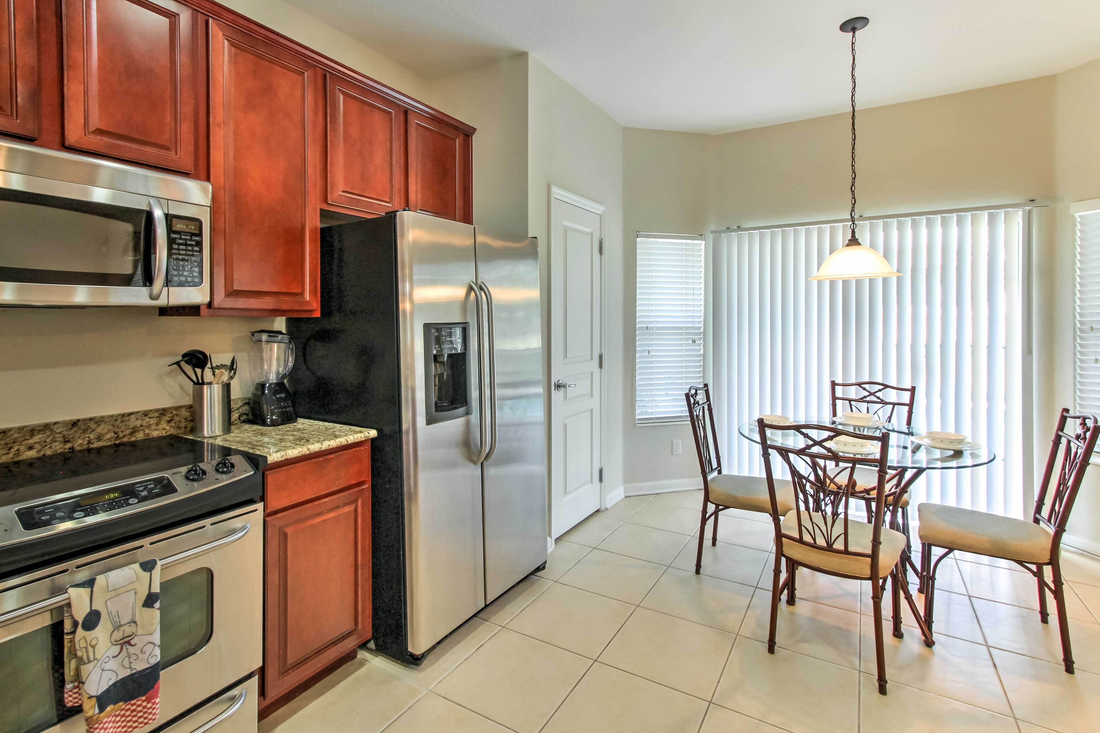 A kitchen with wooden cabinets, stainless steel appliances, a dining table with chairs, and a window with blinds.