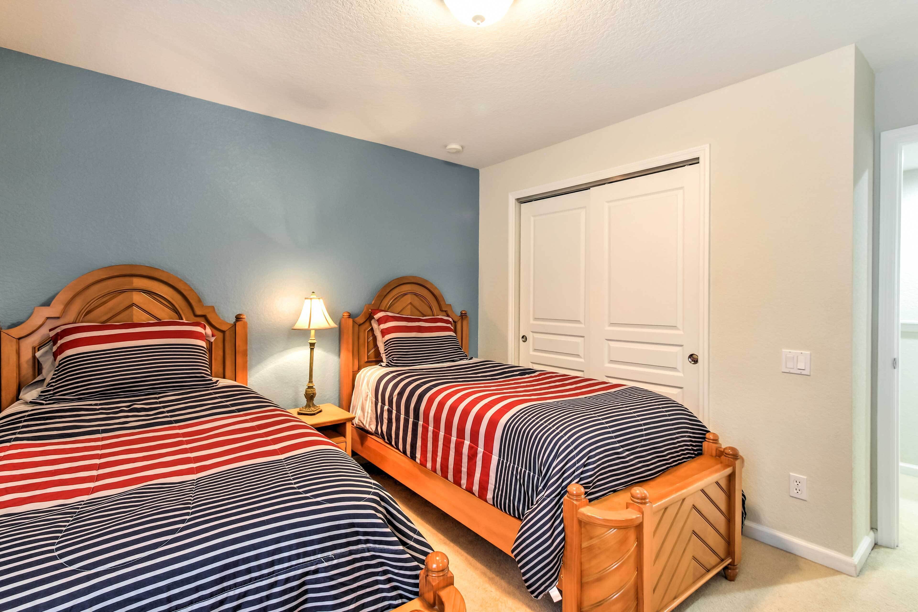Une chambre avec deux lits, une table de chevet avec une lampe, une tête de lit en bois et une porte.