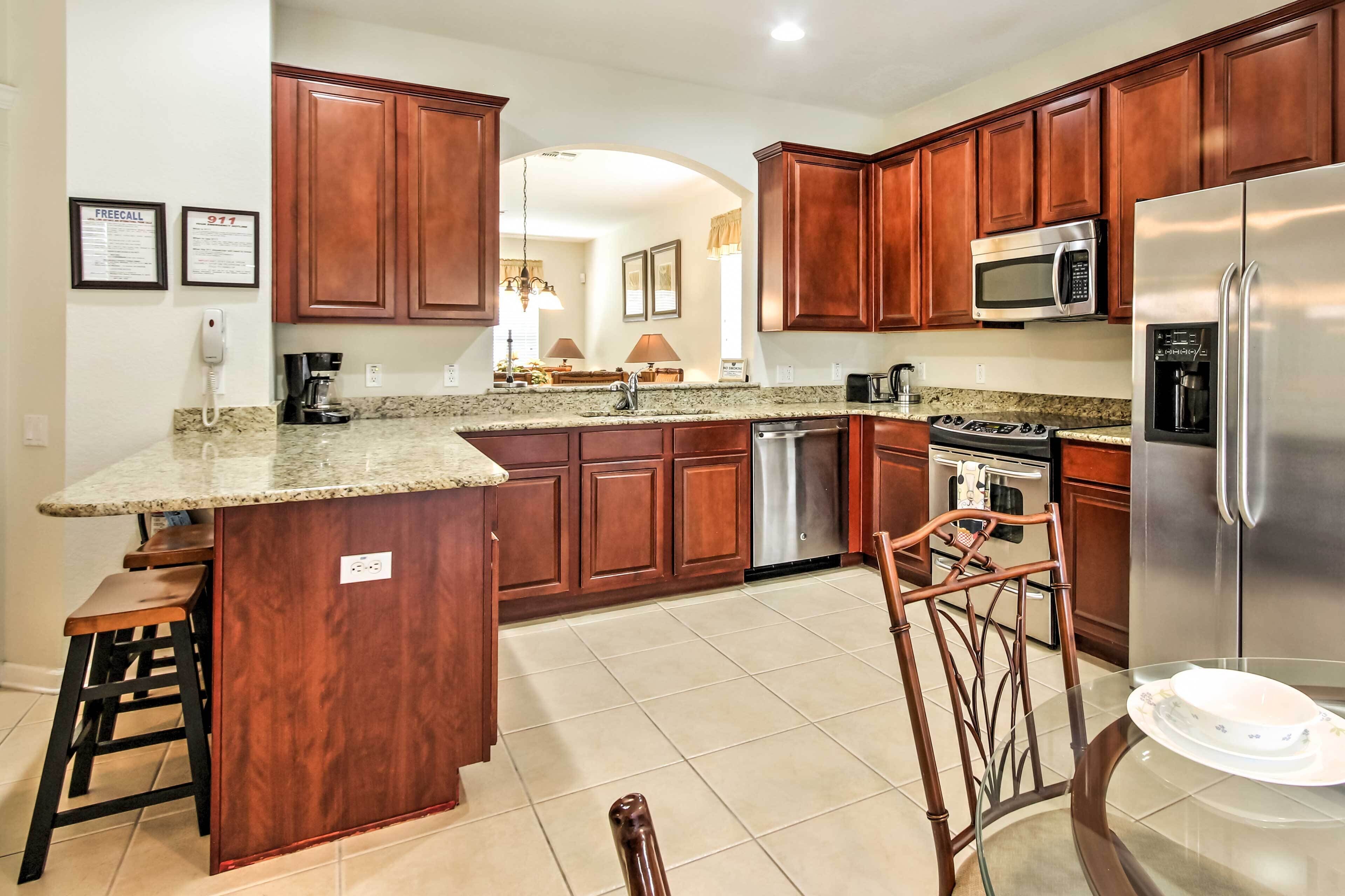 A kitchen with wooden cabinets, granite countertops, stainless steel appliances, and a bar stool.
