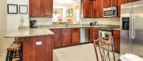 A kitchen with wooden cabinets, granite countertops, stainless steel appliances, and a bar stool.