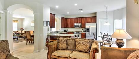 A spacious living room with a large sofa and a coffee table, a kitchen with wooden cabinets and modern appliances, and a dining area with a table and chairs.