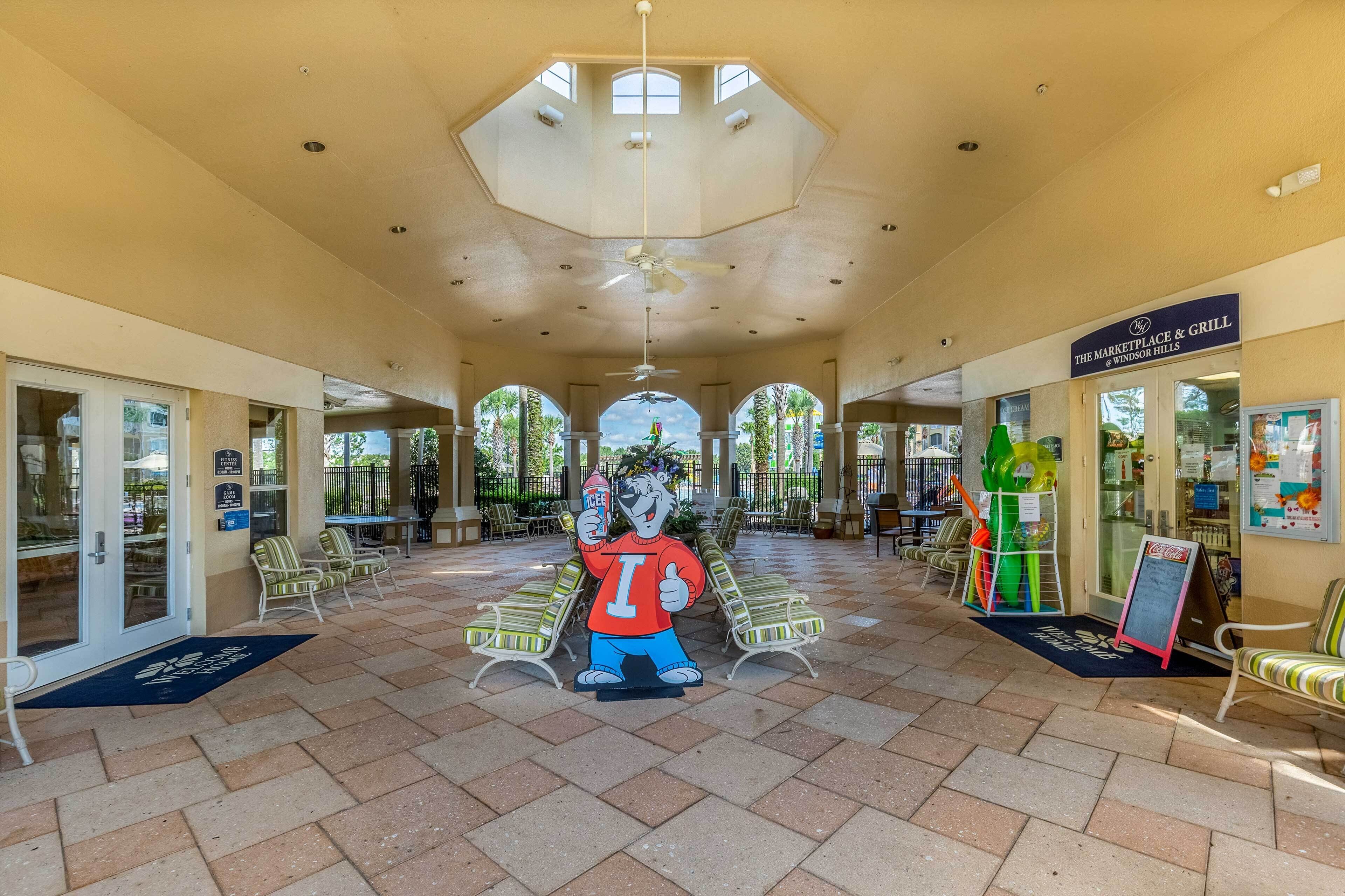 A covered outdoor area with a ceiling fan, lounge chairs, and a mascot holding a drink.
