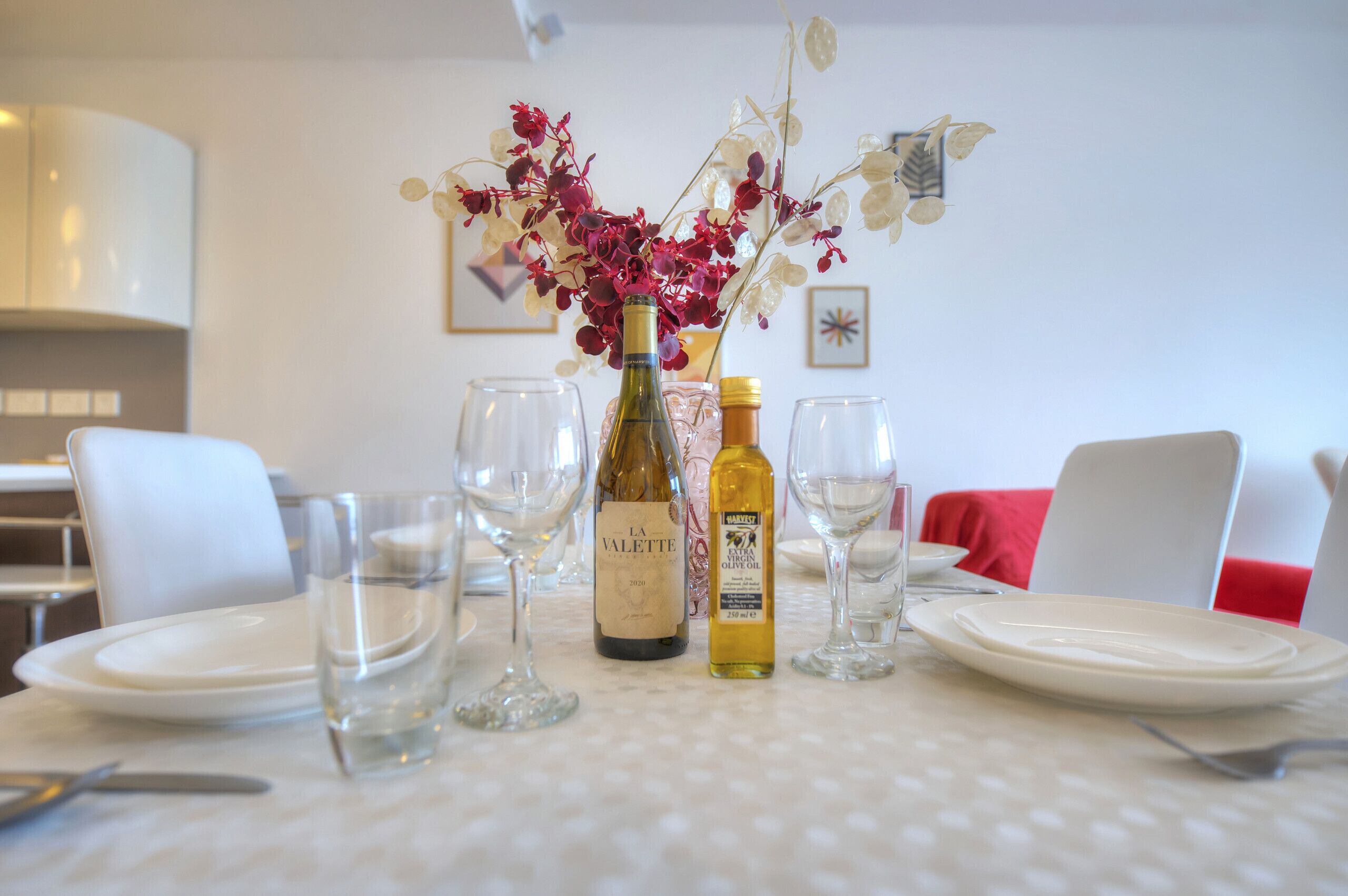 Una mesa de comedor con una botella de vino, una botella de aceite de oliva y un jarrón de flores.