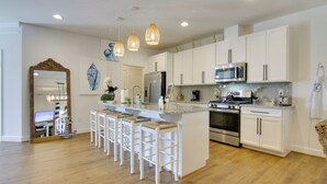 A modern kitchen with white cabinets, a central island with bar stools, stainless steel appliances, and pendant lighting. - Ocean View Home w/ Beach Shuttle, 5 Mi to Coast! (Frankford)
