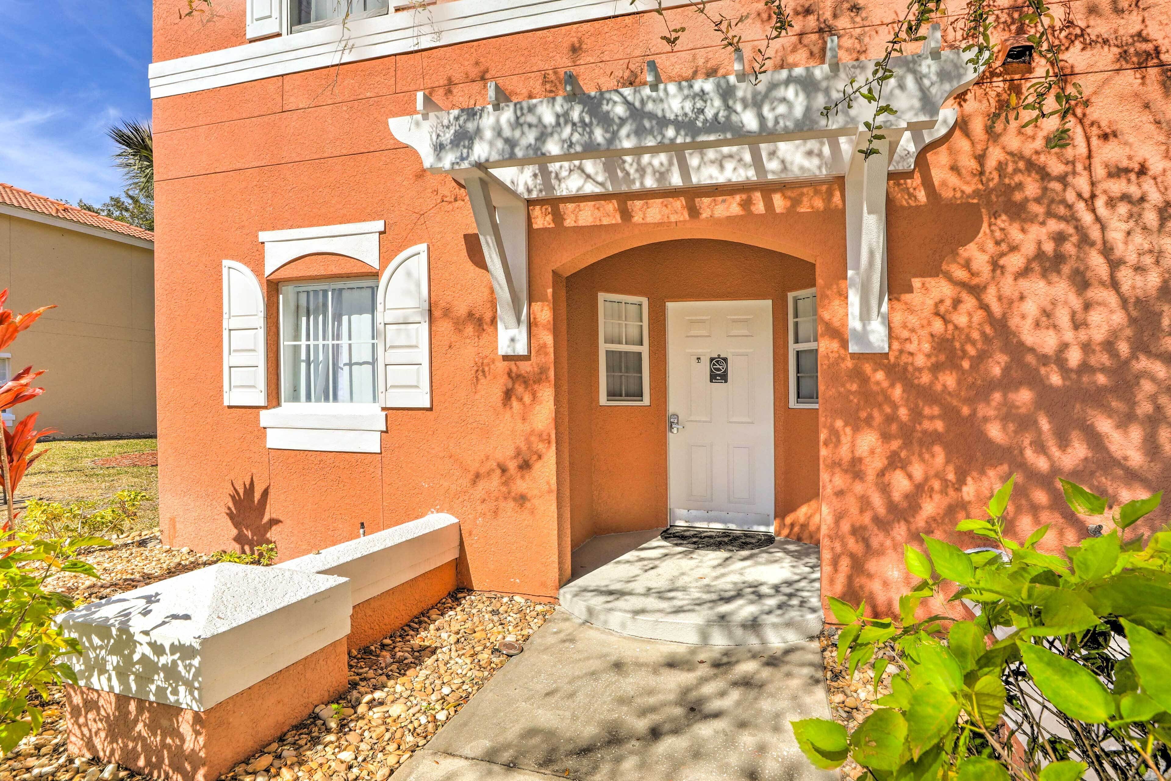 A building with a white door, a white porch, and a small garden area with plants and a concrete bench.