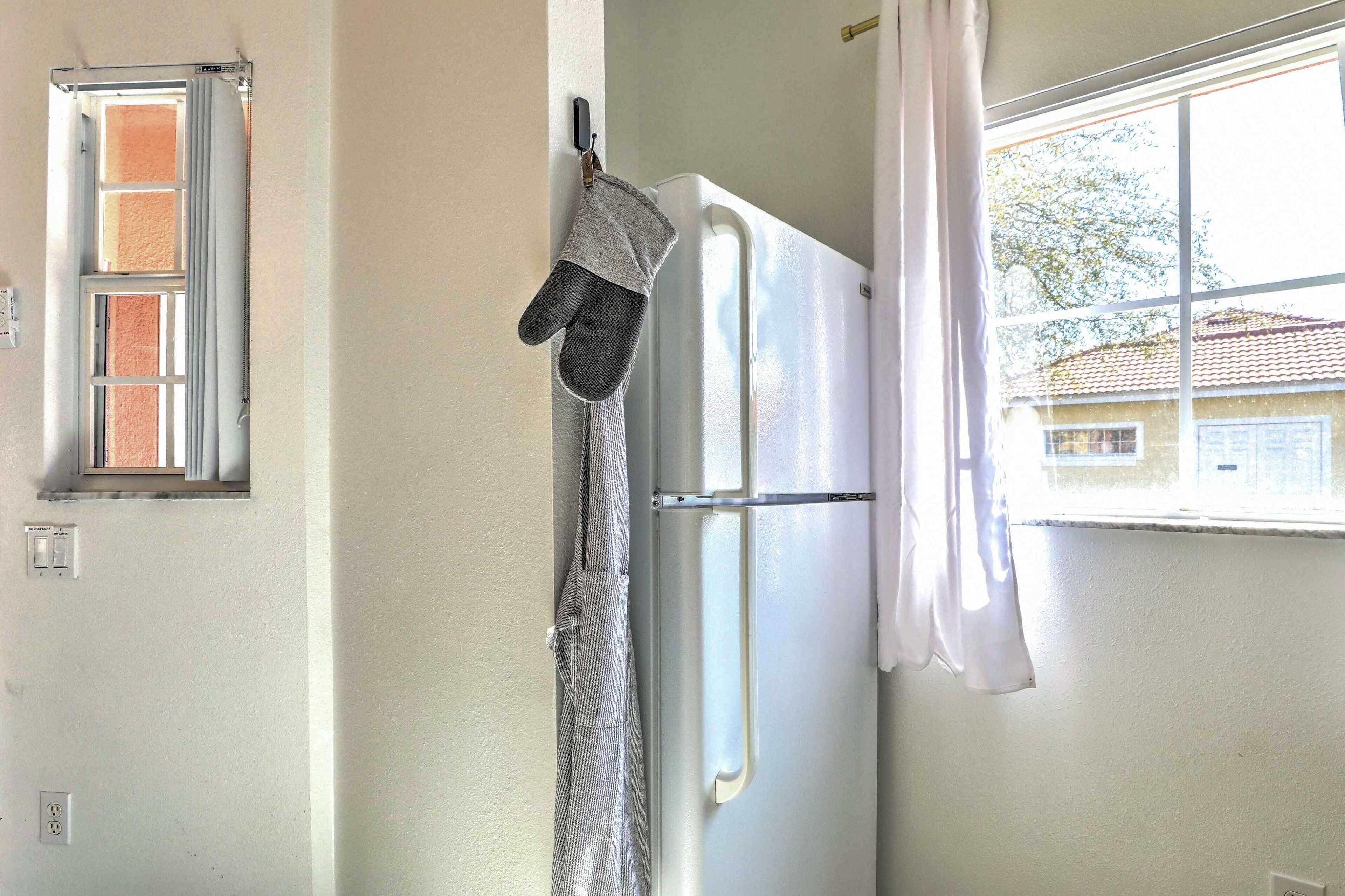 Une cuisine avec un réfrigérateur blanc, une fenêtre donnant sur des immeubles et un manique suspendu.