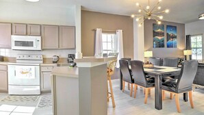 A modern kitchen with white appliances, a central island, and a dining area with a black table and chairs. - Fire Pit + Pool Access: Resort Getaway Near Disney (Kissimmee)