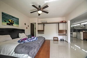 A modern bedroom with a bed, a ceiling fan, a painting, and a view into the kitchen. - Casa Esmeralda w/ Pool Access & Furnished Patio! (Tulum)