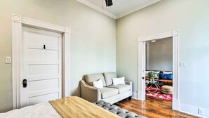 A bedroom with a bed, a grey sofa, and a red rug. - Historic Galveston East End Vacation Rental! (Galveston)