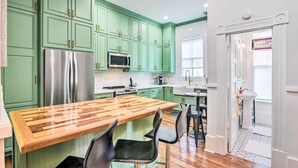 A kitchen with green cabinets, a wooden island, stainless steel appliances, and a view to the adjacent bathroom. - Historic Galveston East End Vacation Rental! (Galveston)