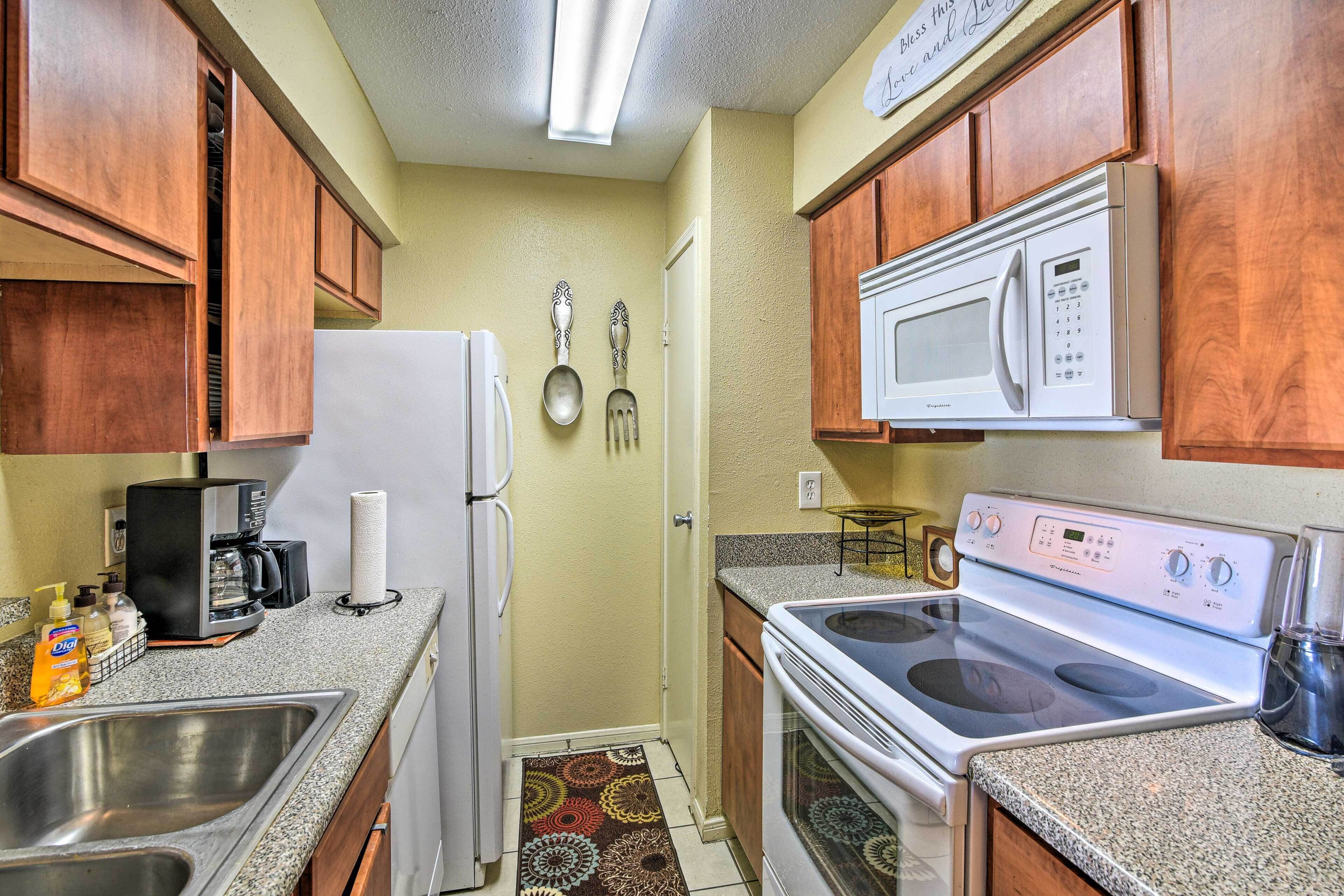 A compact kitchen with wooden cabinets, a white refrigerator, a microwave, a stove, and a coffee maker.
