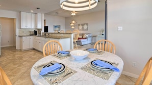 Une cuisine moderne avec des meubles blancs, un plan de travail en granit et un coin repas agrémenté d’une table en marbre pour quatre personnes.