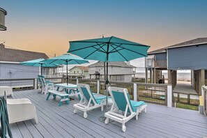 Eine Terrasse mit weißen und türkisblauen Liegestühlen und Sonnenschirmen mit Blick auf einen Strand.