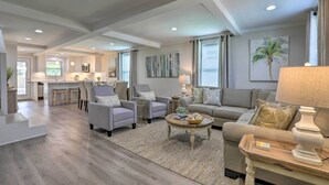 A spacious living area with a sofa, armchairs, and a coffee table. There is a kitchen in the background and a dining area with stools. - Walk to Beach: Home in Galveston! (Galveston)