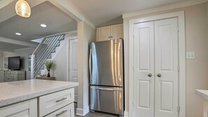 A modern kitchen with white cabinetry, a stainless steel refrigerator, and a wooden floor. - Walk to Beach: Home in Galveston! (Galveston)