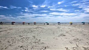 Una playa con filas de sillas y sombrillas bajo un cielo despejado.