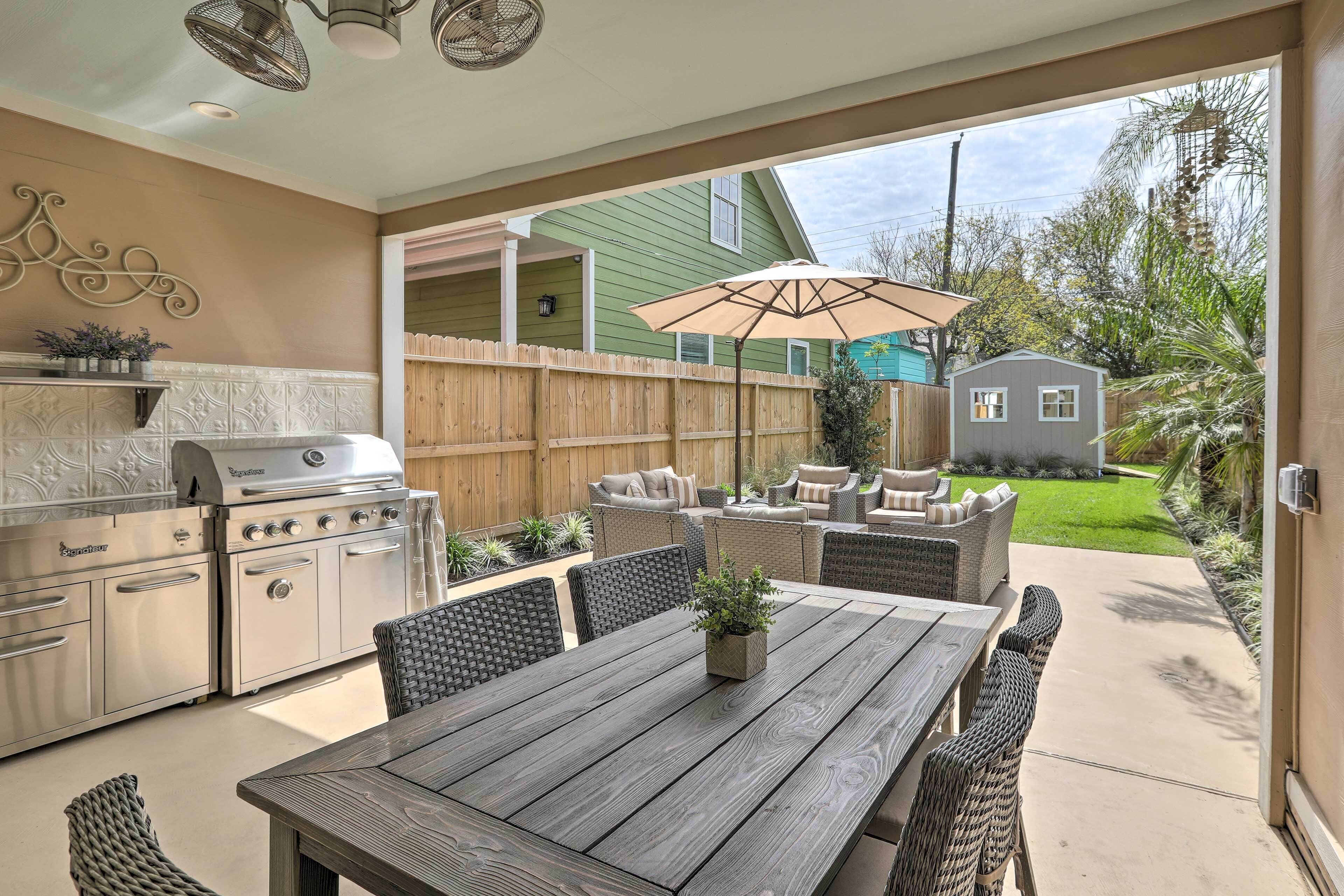 An outdoor patio with a wooden table, wicker chairs, a grill, and a small shed in the background.