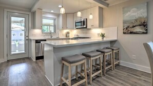 A modern kitchen with a large island, bar stools, pendant lighting, and a microwave. - Walk to Beach: Home in Galveston! (Galveston)