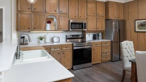 A kitchen with wooden cabinets, stainless steel appliances, a white countertop, and a dining area with a chair.
