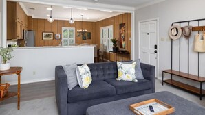 A modern living room with a grey sofa, a wooden coffee table, and a kitchen area in the background.