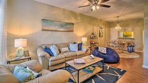 A living room with a beige sofa, a coffee table, a bean bag, and a ceiling fan. - < 1 Mi to Stewart Beach: Gem in East End Galveston (Galveston)