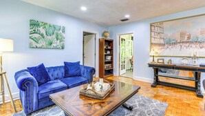 Uma sala de estar com um sofá azul, uma mesa de centro com objetos decorativos, uma estante de livros e um quadro na parede.