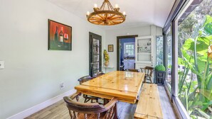Uma sala de jantar com uma mesa e cadeiras de madeira, um candelabro e vista para o verde através de grandes janelas.