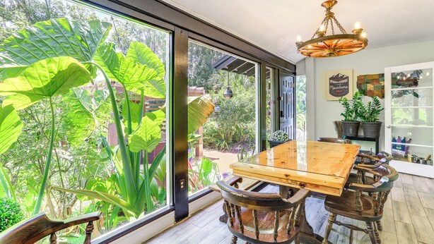 Uma sala de jantar com mesa e cadeiras de madeira, janelas amplas e um lustre.