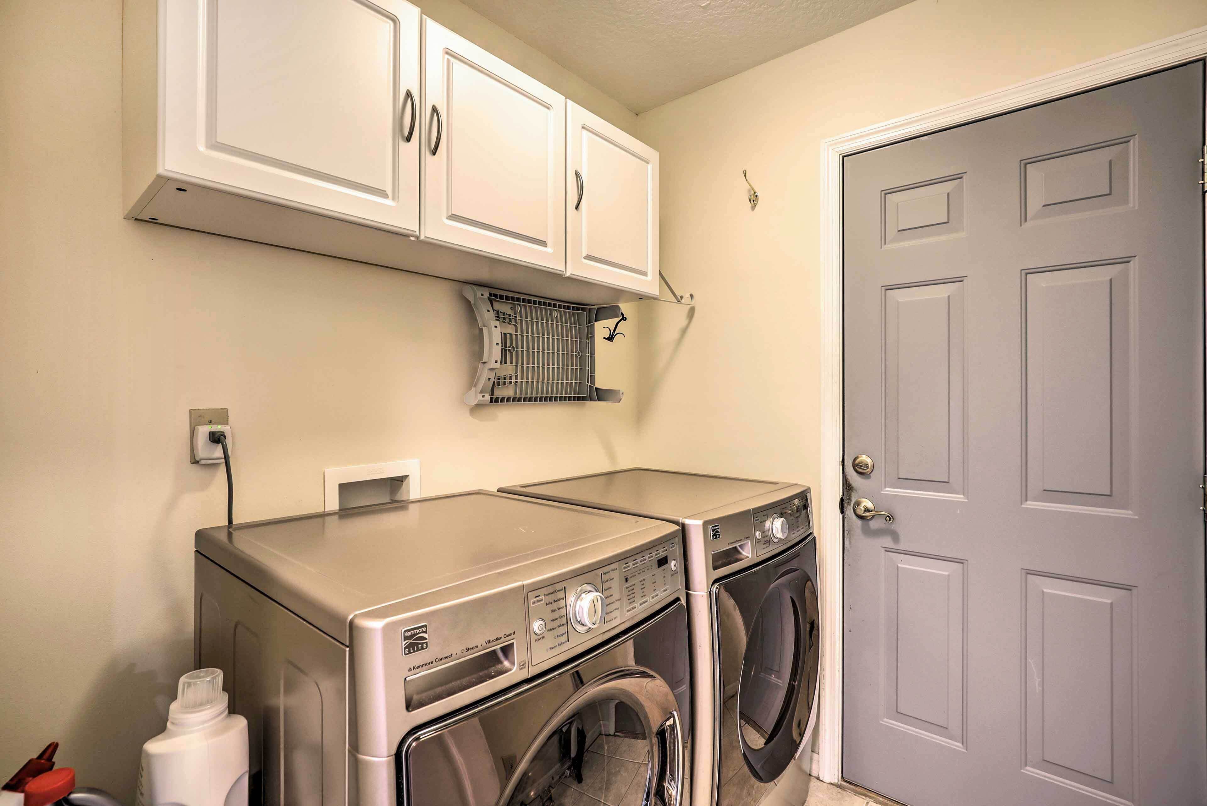 A laundry room with two washing machines and a dryer, a white door, and a white cabinet above the machines.