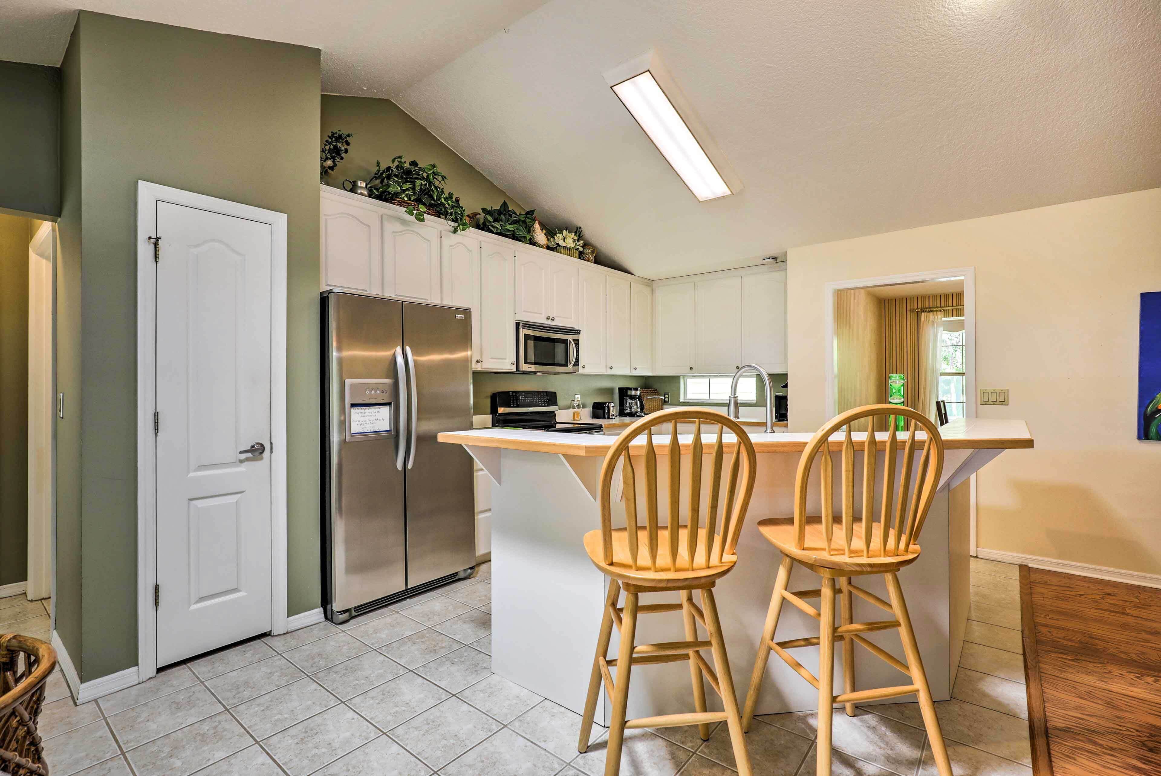 A kitchen with white cabinets, stainless steel appliances, and a wooden island with two chairs.