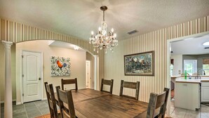 A dining room with a wooden table and chairs, a chandelier, striped wallpaper, and a painting on the wall. - Charming Waldo Getaway Near Lake Santa Fe! (Waldo)