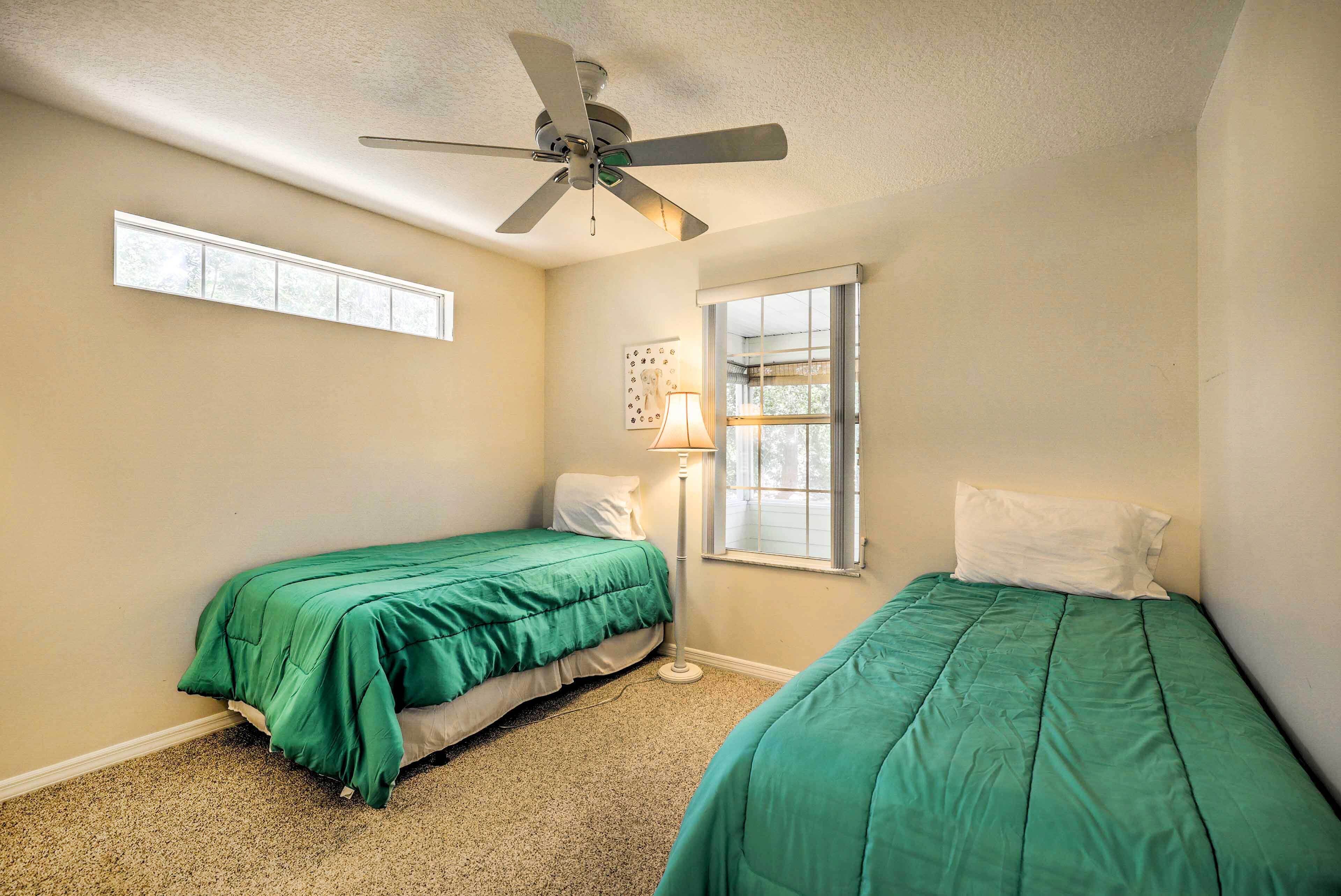 A bedroom with two single beds, a ceiling fan, and two windows.