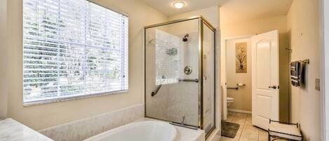 A bathroom with a glass-enclosed shower, a large bathtub, and a window with blinds.