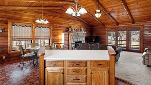 A wooden cabin interior with a kitchen area, dining table, and large windows. - Lakefront Cabin + Guest House Near Granbury Square (Granbury)