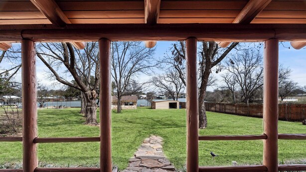 A covered outdoor area with a stone pathway leading to a grassy lawn, surrounded by trees and a wooden fence. - Lakefront Cabin + Guest House Near Granbury Square (Granbury)