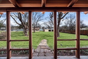 A covered outdoor area with a stone pathway leading to a grassy lawn, surrounded by trees and a wooden fence. - Lakefront Cabin + Guest House Near Granbury Square (Granbury)