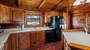 A wooden cabin interior with a kitchen featuring wooden cabinets, a black refrigerator, and a white countertop. - Lakefront Cabin + Guest House Near Granbury Square (Granbury)