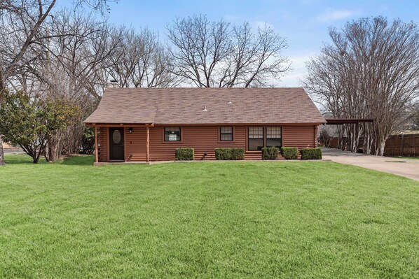 A single-story log cabin with a sloped roof, a front porch, and a small attached garage.