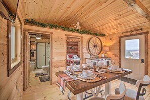 Cozy cabin interior with dining area for four, wooden ceiling, and a bathroom with toilet and sink.
