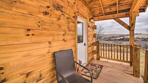 A wooden cabin with a porch, a door, and a view of the landscape.