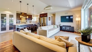 A modern living room with a sofa, a dining area with a kitchen in the background, and a large window providing natural light. - Kona Coast Hideaway w/ Patio & Pacific Ocean Views (Kailua-Kona)