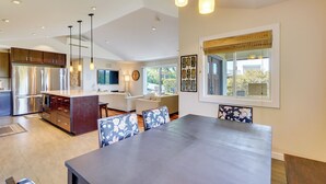 A modern kitchen with a central island, dining area with a large table, and a living space with a sofa and TV. - Kona Coast Hideaway w/ Patio & Pacific Ocean Views (Kailua-Kona)